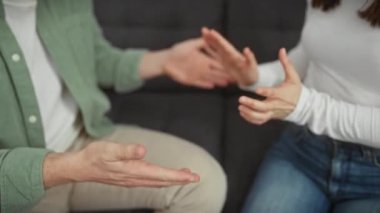 Bir erkek ve bir kadın, kapalı bir oturma odasında el hareketleriyle etkileşime girer ve bir çiftin içindeki bir anlık iletişimi yakalar..