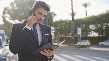 Takım elbiseli profesyonel bir adam güneşli bir şehir sokağında tablet ve telefon ile birden fazla iş yapıyor..