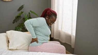 Saçları örgülü Afrikalı Amerikalı bir kadın bir klinikte yatağında sırt ağrısı çekiyor..