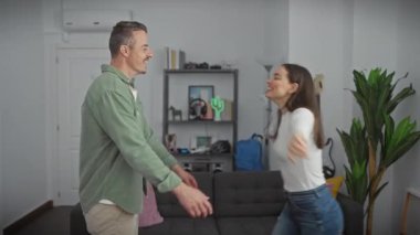 Kot pantolonlu neşeli bir kadın modern bir oturma odasında yeşil hırka giyen gülen bir adama sarılır..