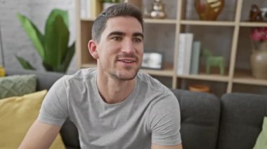 Modern bir oturma odasında sakallı yakışıklı bir genç adam gülümsüyor..