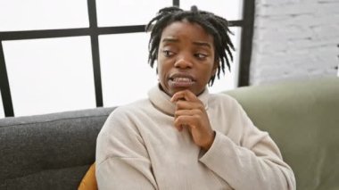 Gergin, genç, siyah bir kadın. Rastalı, rahat bir şekilde kanepede oturuyor. Endişeli. Derin düşüncelere dalmış düşünceli Afrikalı bir yetişkin..