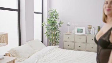 Kısa sarı saçlı, güzel beyaz bir kadın rahat bir yatak odasındaki bir yatakta baştan çıkarıcı pozlar veriyor..