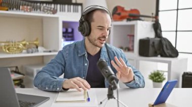 Kot gömlekli kel bir adam, parlak, modern bir stüdyoda beyaz bir masada mikrofon kullanarak podcast yapıyor..