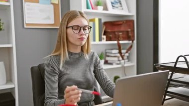 Modern bir ofiste çalışırken gözlüklü beyaz bir kadın komik bir ifade takınıyor.