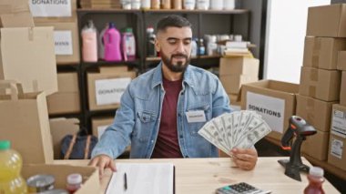 Bağış merkezinde gönüllü olarak çalışan yakışıklı bir adam elinde karton kutularla arka planda para tutuyor..