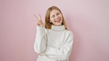 Kazanan titreşimler aşırı yükleniyor! Güzel sarışın kız gülümsüyor, zafer işareti yapıyor, pembe izole duvardan sana küstahça göz kırpıyor. Kendine güvenen, pozitif auralı bir kadın. Bulaşıcı..