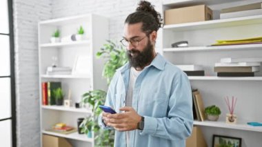 Yakışıklı, sakallı, İspanyol asıllı genç adam modern ofis içinde telefonu tutarken başparmağını kaldırıyor.