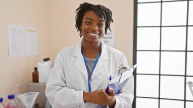 Afrika kökenli Amerikalı kadın doktor elinde bir panoyla laboratuvar ortamında gülümsüyor.