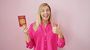 Coşkulu genç sarışın kadın, Kuzey İrlanda pasaportuyla izole edilmiş pembe arka planı onaylıyor.