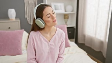 Pijamalı bir kadın rahat bir yatak odasında kulaklıkla müzik dinlemekten hoşlanır.