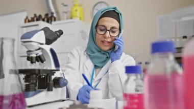 Bir laboratuvar ortamında notlar yazarken tesettürlü profesyonel bir kadın bilim adamı bir telefon konuşmasında yer aldı..