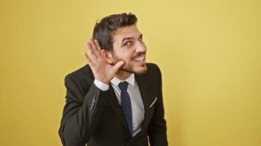Şık, genç İspanyol bir adam, takım elbiseli bir patron, sulu dedikoduları dinliyor. Hevesle dinleyen, elle kavrayan, dikkatle dinleyen, sadece mırıltıyı duymayan. İzole edilmiş sarı arka planda mutlu bir dedikodu alıcısı.