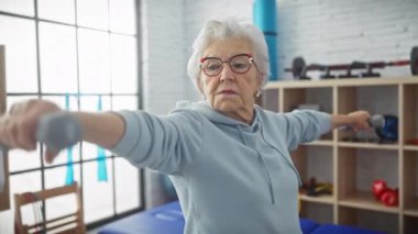 Üst düzey kadın, rehabilitasyon salonunda dambıllarla egzersiz yapıyor. Fizyoterapi ve fitness üzerine odaklanıyor.