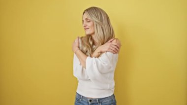 Radiant young blonde woman shares a joyful hug with herself! exuding happy confidence, she poses against a vibrant yellow background. a portrait of self love and egoistic pleasure.