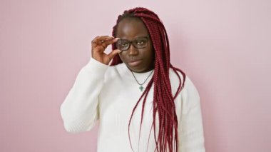 Saçları örgülü düşünceli bir Afrikalı kadın pembe bir duvara gözlük takıyor.