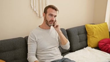 Orta yaşlı bir adam sıcak oturma odasında telefonla konuşurken termometreye bakar.