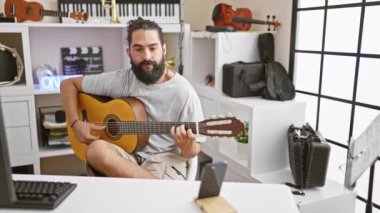 Modern bir müzik stüdyosunda gitar çalan sakallı yakışıklı bir İspanyol.