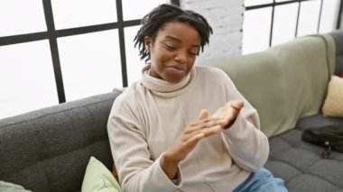 Sinsi ama muzaffer, rastalı genç siyah kadın rahat rahat rahat rahat rahat rahat rahat rahat rahat rahat rahat rahat kanepede dinleniyor ve elleriyle sinsi bir para hareketi yapıyor. Maaş ödeme başarısını gösteren ev yapımı bir milyoner..