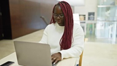 Ofis ortamında örgü ören ve bardakları çıkaran Afro-Amerikalı kadın, profesyonellik ve rahatlık saçıyor..