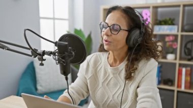 İspanyol kadın stüdyodan mikrofon, kulaklık ve dizüstü bilgisayarla podcast yayınlıyor.