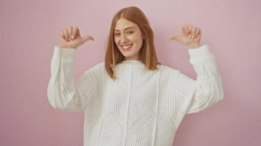 Neşeli, genç, kızıl saçlı bir kadın tek başına dikiliyor, izole pembe arka planda gururla kendini işaret ediyor. Güzel bir yüz ifadesi, rahat bir süveter giyme, kendine güvenen mutluluk tanıtımı..