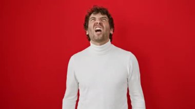Sinirli, genç İspanyol bir adam, kızgın ve öfkeli, ıstırap içinde bağırıyor. Kazak giyiyor, izole edilmiş kırmızı zemine karşı duruyor. İfade ham öfke ve hayal kırıklığını gösterir.