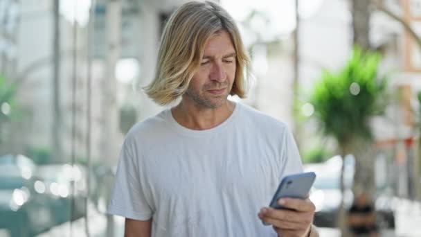 Bonito Homem Adulto Com Longos Cabelos Loiros Olhando Para Smartphone — Vídeo de Stock