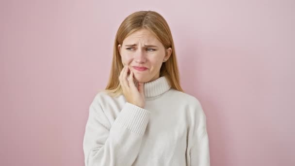 ゴージャスなブロンドの少女 痛みを伴う表情 歯痛を患っている口の上に手を渡す 歯の病気のために必要とされる歯科医 ピンクの背景に対して単独で立っています — ストック動画