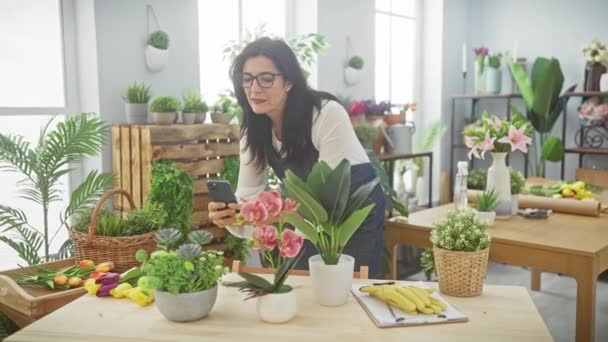 Іспаномовна Жінка Використовує Смартфон Магазині Приміщенні Оточеному Рослинами Природним Світлом — стокове відео
