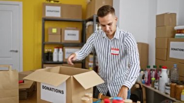 Delikanlı, etiketli kutuları olan bir depoda bağış organize ediyor, içeride gönüllü çalışıyor.