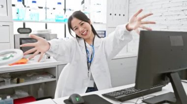Beyaz laboratuvar önlüklü neşeli Çinli kadın bilim adamı, kolları açık kameraya ışıldıyor, laboratuvarda rahatlatıcı bir kucaklamaya hazır. Neşeli mutluluk ve başarının vücut bulmuş hali..