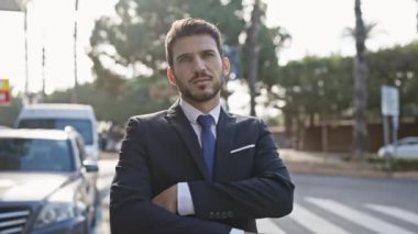 Kendine güvenen, takım elbiseli İspanyol bir adam güneşli şehir caddesinde kollarını kavuşturdu.