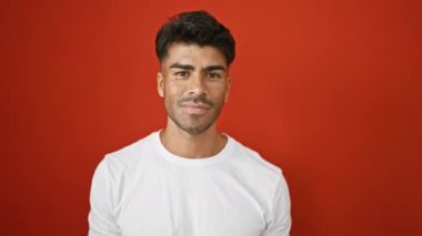 Beyaz gömlekli yakışıklı adam kırmızı bir duvara karşı poz veriyor, elinde kırmızı bir kalp, pozitif duygular ve kendine güven gösteriyor..