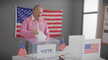 Orta yaşlı bir adam, arka planda Amerikan bayrağı olan bir Amerikan seçim merkezinde oy kullanıyor..