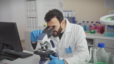 Modern laboratuvar ortamında mikroskop altında numuneleri inceleyen sakallı bilim adamı..