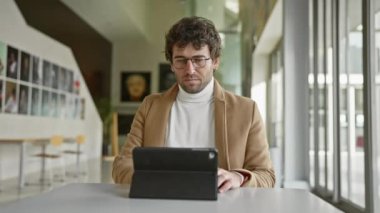 Ofiste sakallı, tablet kullanarak gözlük takan yakışıklı bir İspanyol.