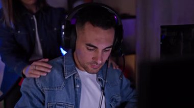 Loş aydınlatılmış bir oyun odasında, kulaklık takan odaklanmış bir adam, bir kadından destek dokunuşu alıyor, arkadaşlığı ve boş zamanları gösteriyor..