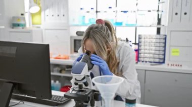 Parlak, modern bir laboratuvar ortamında mikroskop kullanan kendinden emin genç bir kadın bilim adamı..