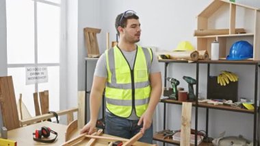 İki adam atölyede, biri yansıtıcı yelek, diğeri ekose gömlek giymiş, marangozluk projesi için el sıkışıyorlar..
