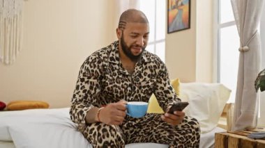 Leopar pijamalı rahat bir adam güneşli odasında kahve ve akıllı telefondan hoşlanır..