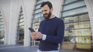 Neşeli sakallı adam şehir merkezinde akıllı telefondan iyi haberleri kutluyor.