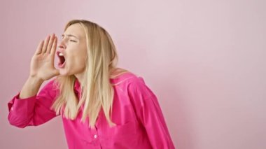 Şaşkınlık içinde kaybolmuş genç sarışın kadın pembe izole edilmiş arka planda dururken omuz silkiyor. Kolları açık ve kararsız.