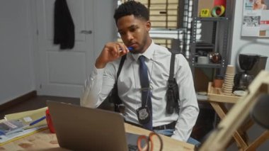 Ofiste, suç delillerini dizüstü bilgisayarla analiz eden düşünceli bir Afro-Amerikan erkek dedektif..