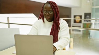 Modern ofiste dizüstü bilgisayarla çalışırken, örgü ören siyah bir kadın boyun ağrısı çekiyor..