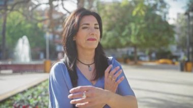 Güneşli bir parkta kollarını kavuşturmuş kendinden emin, olgun bir İspanyol kadın..