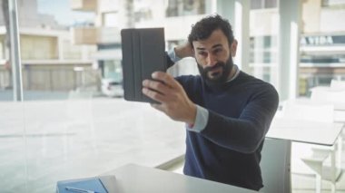 Yakışıklı, orta yaşlı, sakallı bir adam. Tabletle selfie çekiyor. Teknoloji ve iş hayatını karıştırıyor..