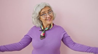 Gri saçlı, orta yaşlı, gururla kendini gösteren, pembe arka planda duran, mutlu bakışlı gözlük takan bir kadın..