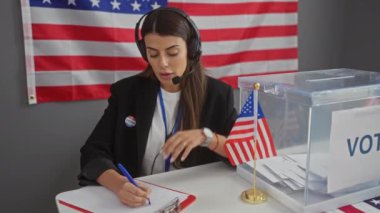 Kulaklık takan genç bir kadın ve Amerika Birleşik Devletleri seçim sürecinde Amerikan bayrağı altında yardım ediyor..