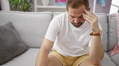 İçerideki gri koltukta düşünceli bir şekilde oturan, stresi ya da baş ağrısını tasvir eden olgun İspanyol bir adam..